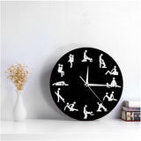 Horloge murale position sexuelle Kama Sutra noire avec silhouettes et aiguilles blanches, posée comme objet de décoration sur une table basse dans un salon moderne.