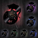 Un panneau mural de présentation montrant sept variations d'une même horloge vinyle (chat et bocal de poisson), montée sur un mur en planches de bois sombres. L'image principale montre un rétroéclairage rouge, tandis que six miniatures affichent des couleurs d'éclairage LED différentes (rose, vert, violet, etc.).