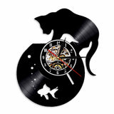 Horloge murale design fabriquée à partir d'un disque vinyle noir recyclé. La découpe représente un chat noir stylisé marchant au-dessus d'un bocal rond contenant un poisson rouge et des bulles. Le cadran central possède des chiffres arabes blancs et un mécanisme d'engrenages visible.